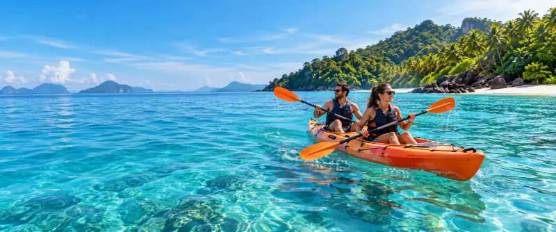Kayakers in buoyancy vests exploring clear island waters beside a tropical shore.